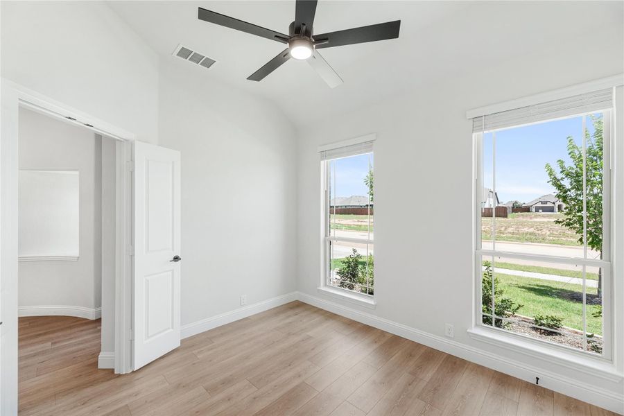 Empty bedroom with vaulted ceiling, ceiling fan, hardwood floors, and two windows with yard views