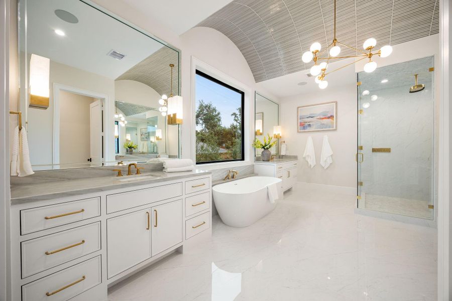 A luxurious primary bathroom designed with a spa-like ambiance, featuring expansive dual vanities, elegant finishes, and abundant natural light. Clean lines and a neutral palette create a calming environment throughout. The highlight of this space is the freestanding soaking tub positioned beneath a large picture window, offering a serene focal point that elevates both relaxation and design.