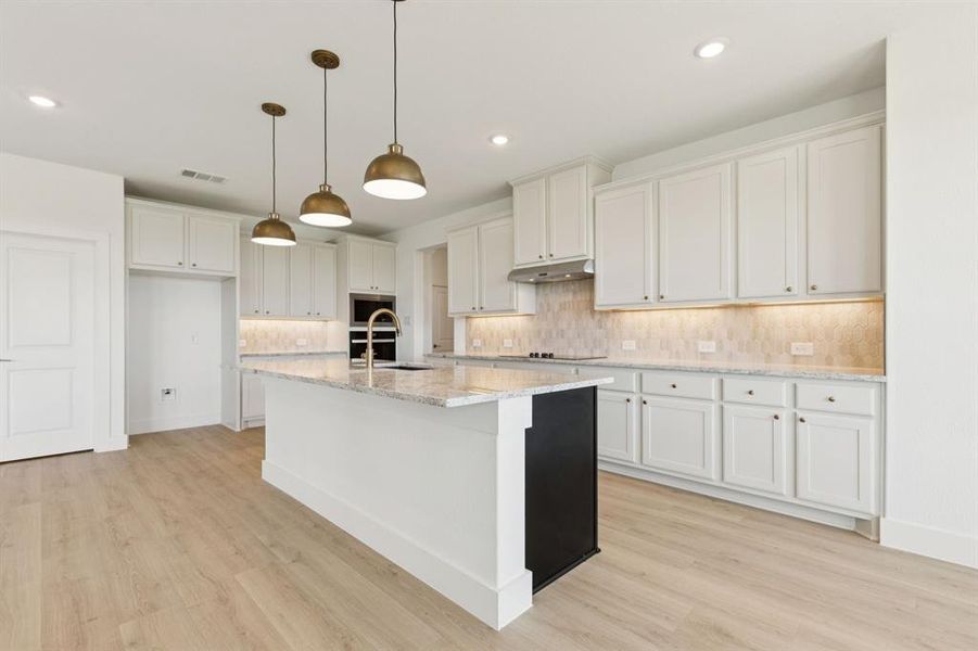 Kitchen featuring decorative light fixtures, tasteful backsplash, a center island with sink, light stone counters, and recessed lighting
