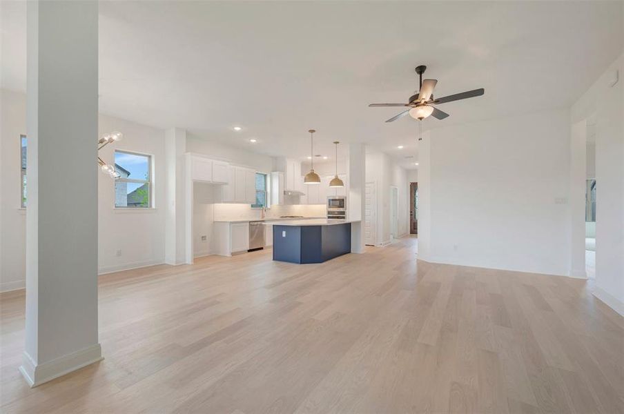 Open-concept living area with light wood-finish flooring, white walls, and a modern ceiling fan