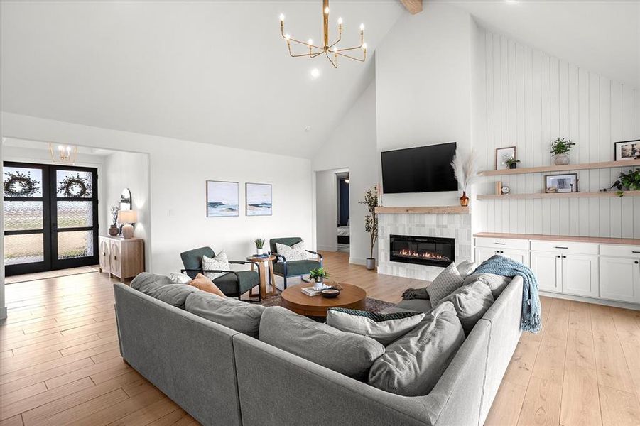 Living room featuring beam ceiling, light wood-type flooring, high vaulted ceiling, and a tiled fireplace