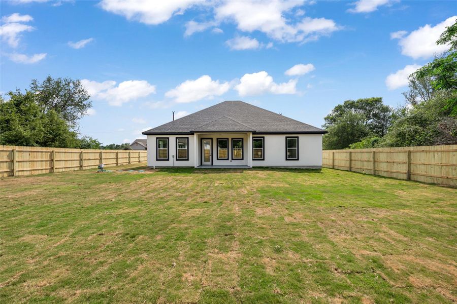 Expansive rear yard featuring a newly installed privacy fence, a newly constructed home exterior with white siding, and a dark shingle roof