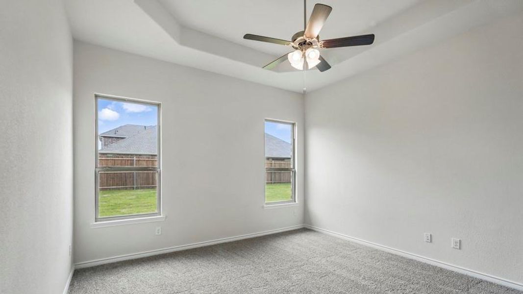 Spacious room featuring a tray ceiling, ceiling fan with integrated lighting, and neutral wall paint