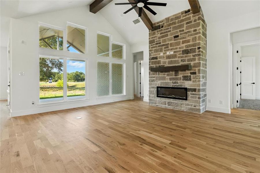 Unfurnished living room with beam ceiling, ceiling fan, high vaulted ceiling, a fireplace, and light wood-type flooring Unfurnished living room with beam ceiling, ceiling fan, high vaulted ceiling, a fireplace, and light wood-type flooring