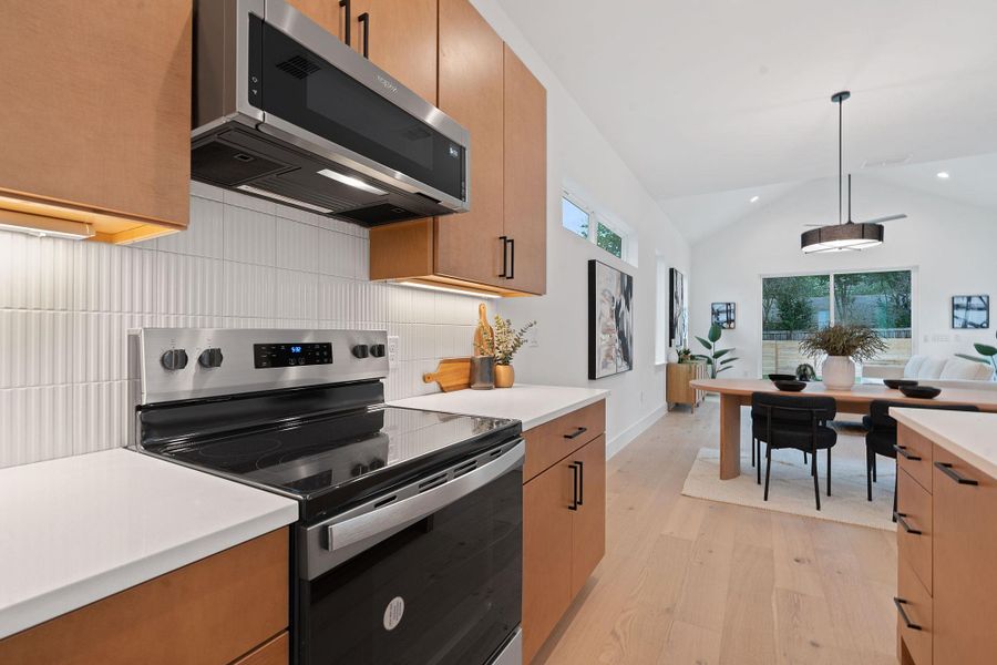 Kitchen with stainless steel appliances, lofted ceiling, light wood-style floors, healthy amount of natural light, and hanging light fixtures Kitchen with stainless steel appliances, lofted ceiling, light wood-style floors, healthy amount of natural light, and hanging light fixtures