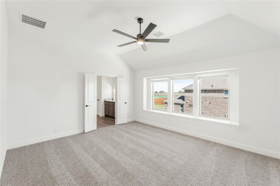 Empty master bedroom with vaulted ceiling, ceiling fan, carpet floors, and ensuite bathroom doorway Empty master bedroom with vaulted ceiling, ceiling fan, carpet floors, and ensuite bathroom doorway