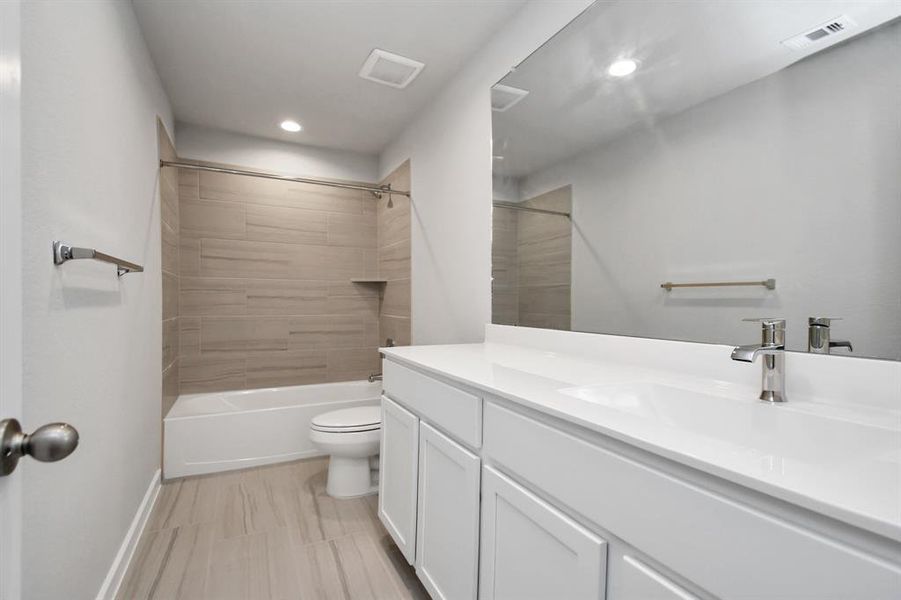 The secondary bath includes modern tile flooring, a combined bath and shower with a tile surround, light wood cabinetry, and a beautiful light-colored countertop. Sample photo of completed home with similar floor plan. Actual colors and selections may vary.