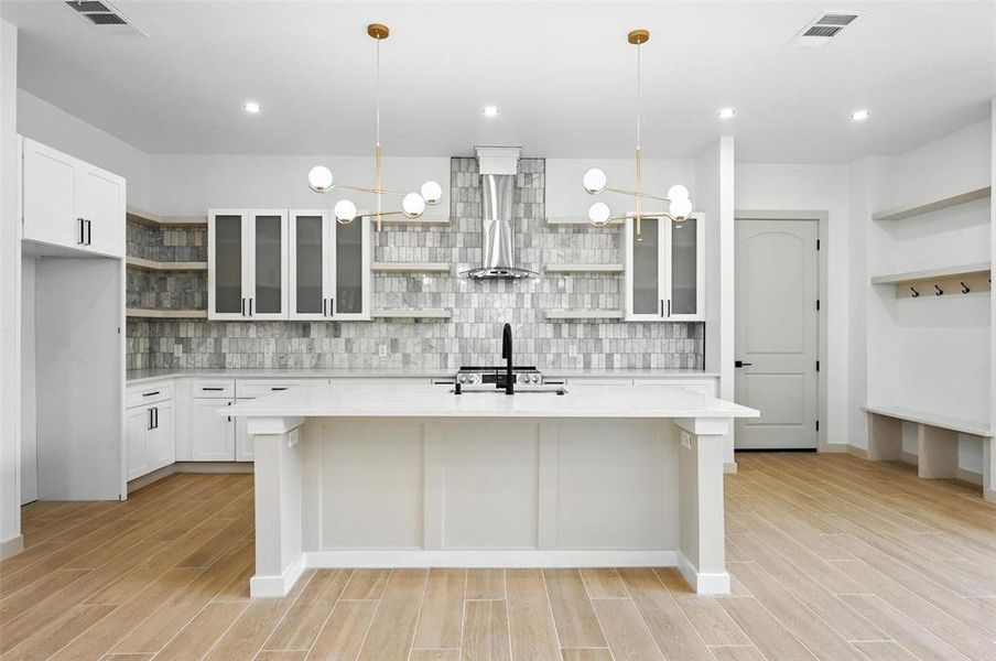 Kitchen with open shelves, light countertops, an island with sink, backsplash, and wood finish floors Kitchen with open shelves, light countertops, an island with sink, backsplash, and wood finish floors