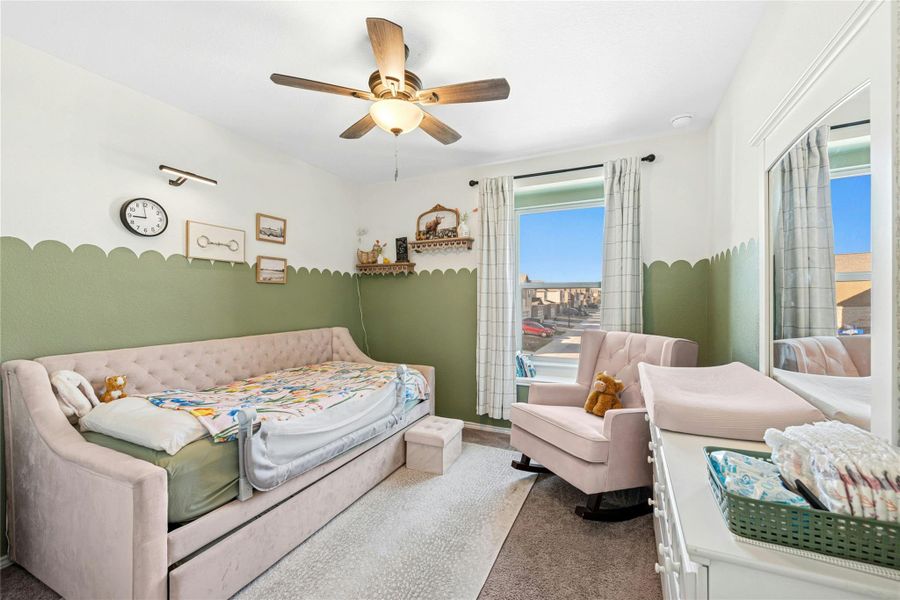 A spacious and inviting bedroom featuring plush carpet flooring, a ceiling fan, custom paint touches, and a large closet. Abundant natural sunlight enhances the room’s warm and comfortable atmosphere.
