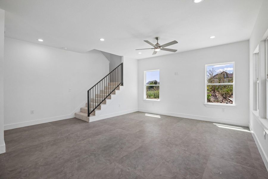 An open living space features durable tile flooring, recessed lighting, and a staircase.