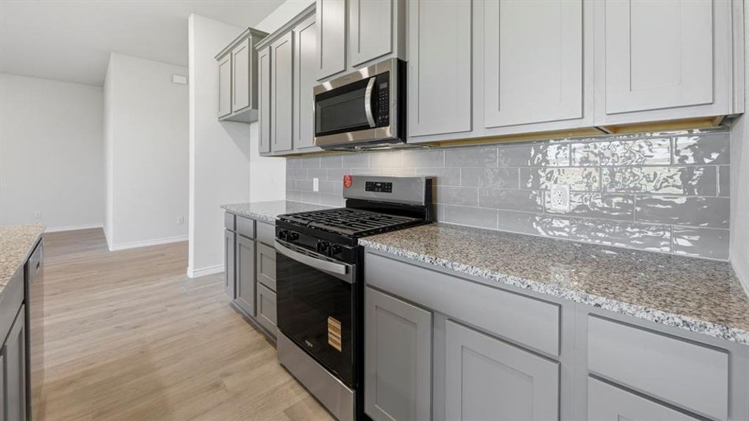 Kitchen with appliances with stainless steel finishes, light wood-style flooring, light stone counters, and decorative backsplash Kitchen with appliances with stainless steel finishes, light wood-style flooring, light stone counters, and decorative backsplash