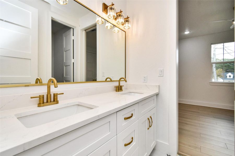 Spa-like dual vanity featuring sleek white quartz countertops and contemporary under-mount sinks. The brushed gold faucets and matching hardware perfectly complement the designer light fixtures and large-scale mirror.