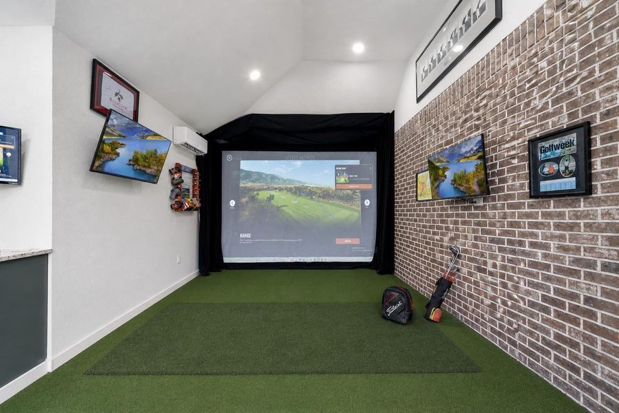 Currently this room features a sleek indoor golf simulator setup with a putting green, wall-mounted screens, and stylish brick accents, perfect for golf enthusiasts.
