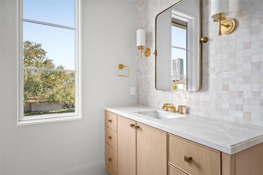 This secondary bathroom features a custom vanity with marble counters, accented by Top Knobs Ascendra honey bronze cabinet hardware and walls adorned with Zellige Desert White tile, which complement the Aerin Drunmore single sconces that provide a warm glow. A shower/tub combo is finished with MLW Cadence and Zellige Desert White tile walls and is paired with a Waterworks Riverun brass shower kit. Underfoot, Roman Tumbled Vanilla limestone tile floors add a timeless touch.