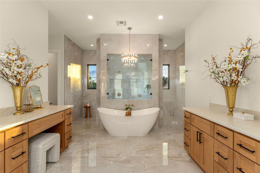 Full bath featuring light marble finish floors, a freestanding bath, a chandelier, and walk in shower