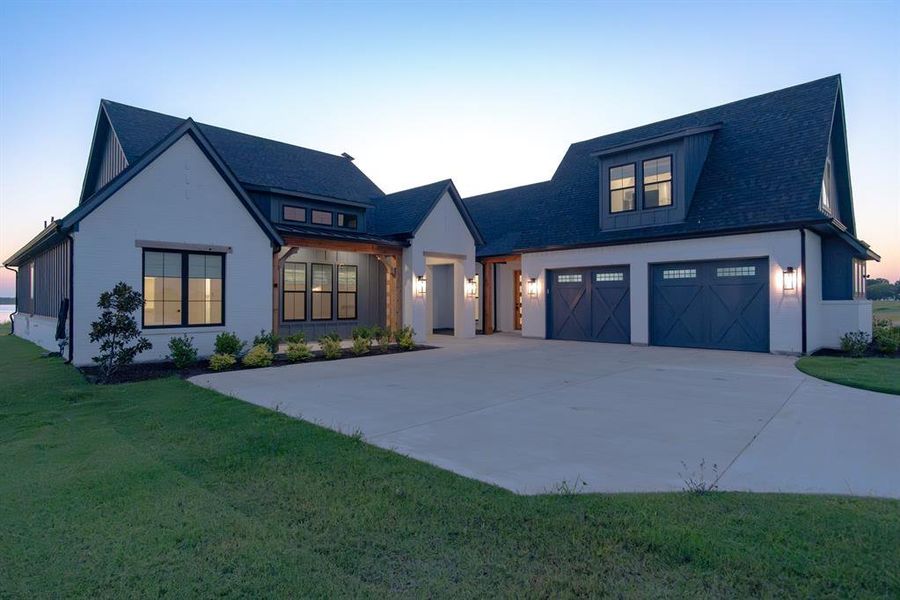 Modern inspired farmhouse with a garage, driveway, a shingled roof, and a yard Modern inspired farmhouse with a garage, driveway, a shingled roof, and a yard