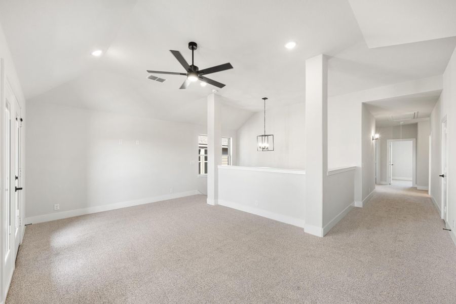 Open upstairs living area with vaulted ceiling, ceiling fan, carpet flooring, and hallway leading to bedrooms