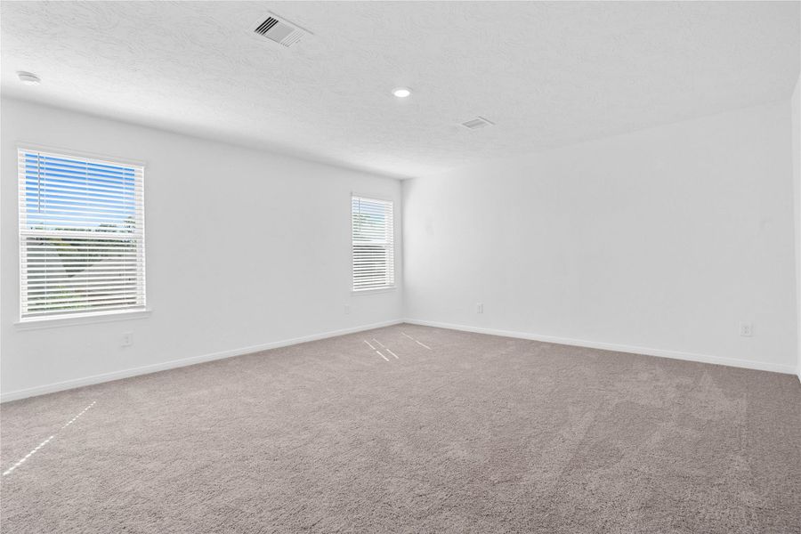 Relax and recharge in this stunning primary suite! This expansive room offers plush carpeting, neutral-toned walls, high ceilings, recessed lighting, large windows fitted with privacy blinds, and an added sitting area—perfect for unwinding after a long day.