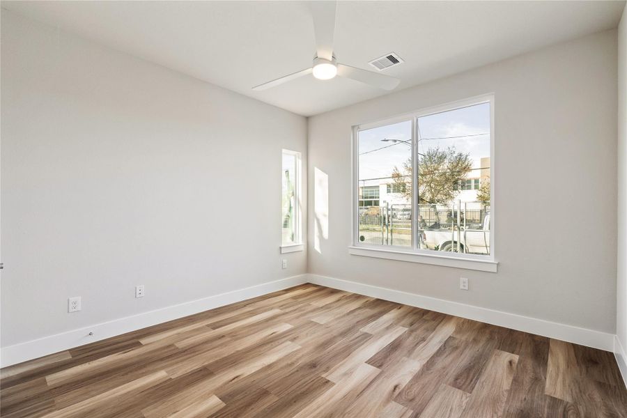 First-floor secondary bedroom with oversized custom windows, ceiling fan, and views of the fully fenced front yard. Bright, quiet, and well-proportioned.