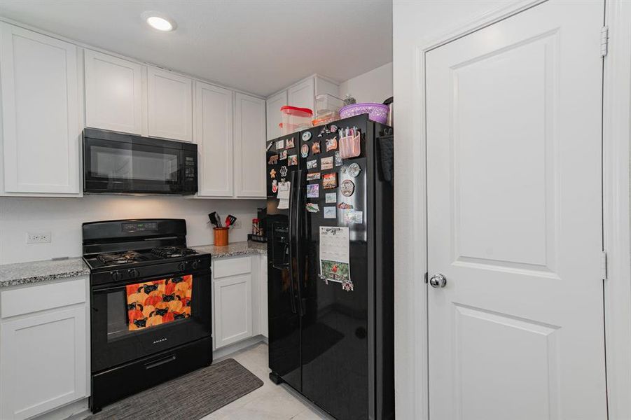 Kitchen with black appliances, white cabinets, light stone countertops, and light tile patterned floors