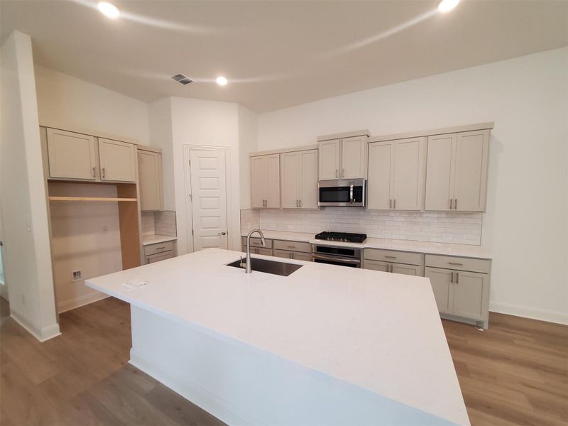Kitchen featuring an island with sink, light wood-style flooring, stainless steel appliances, backsplash, and a sink Kitchen featuring an island with sink, light wood-style flooring, stainless steel appliances, backsplash, and a sink