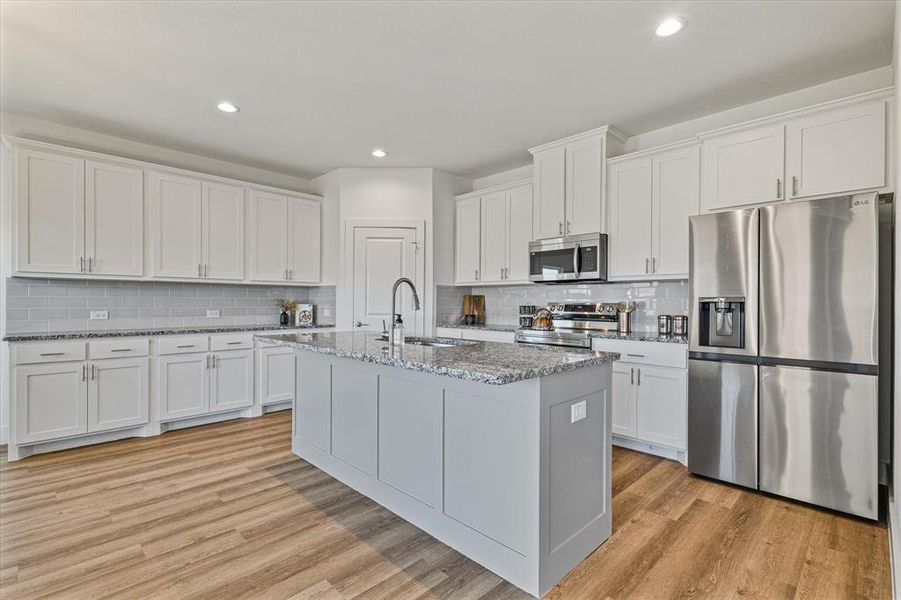 Kitchen with backsplash, white cabinets, light hardwood / wood-style flooring, light stone counters, and stainless steel appliances Kitchen with backsplash, white cabinets, light hardwood / wood-style flooring, light stone counters, and stainless steel appliances
