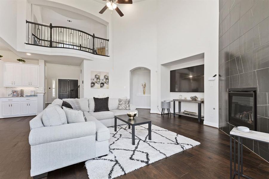 Living room featuring a towering ceiling, ceiling fan, dark hardwood / wood-style flooring, and a tile fireplace