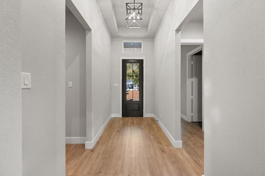 Foyer entrance with light wood finished floors, a textured wall, and a raised ceiling Foyer entrance with light wood finished floors, a textured wall, and a raised ceiling