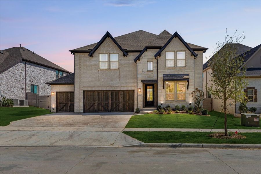 Two-story brick home with wood garage doors, black trim, and landscaped front yard at dusk