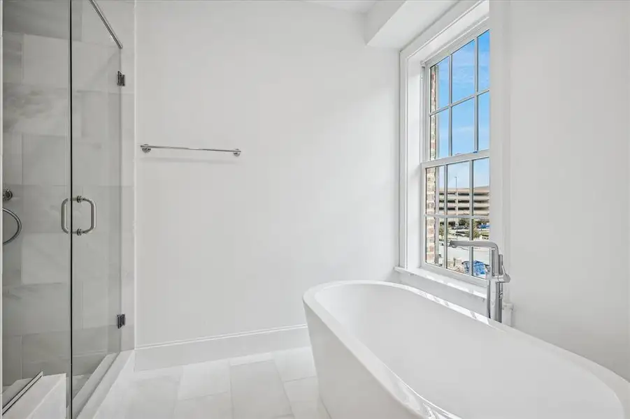 Freestanding soaking tub with chrome floor-mounted filler, accompanied by a large paneled window