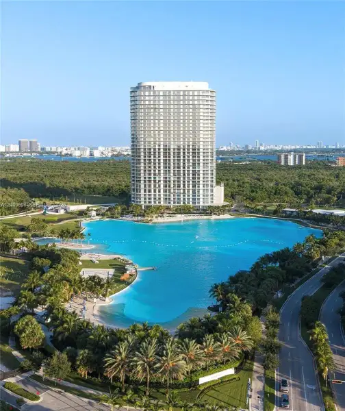 High-rise residential tower featuring floor-to-ceiling windows, expansive man-made lagoon, white sand beaches, and lush tropical landscaping