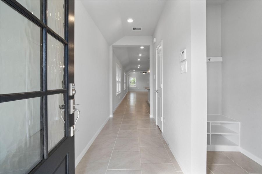 This entryway features a modern, open-concept design. The long, bright corridor utilizes a neutral color palette, recessed lighting, and floor tiles to lead the eye toward the home's main living area.