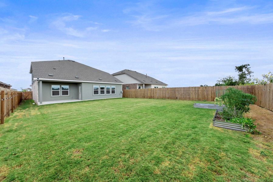 A spacious, green yard awaits, bordered by a privacy fence and featuring raised garden beds. A spacious, green yard awaits, bordered by a privacy fence and featuring raised garden beds.