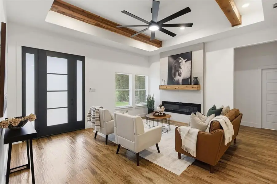 Spacious living area featuring wood-finish flooring, a modern linear fireplace with a light-toned tile surround, and an exposed beam ceiling