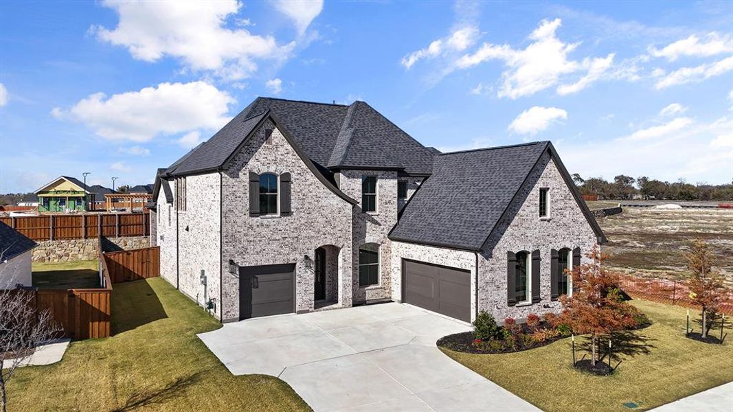 French country inspired facade with brick siding, concrete driveway, a shingled roof, and a garage
