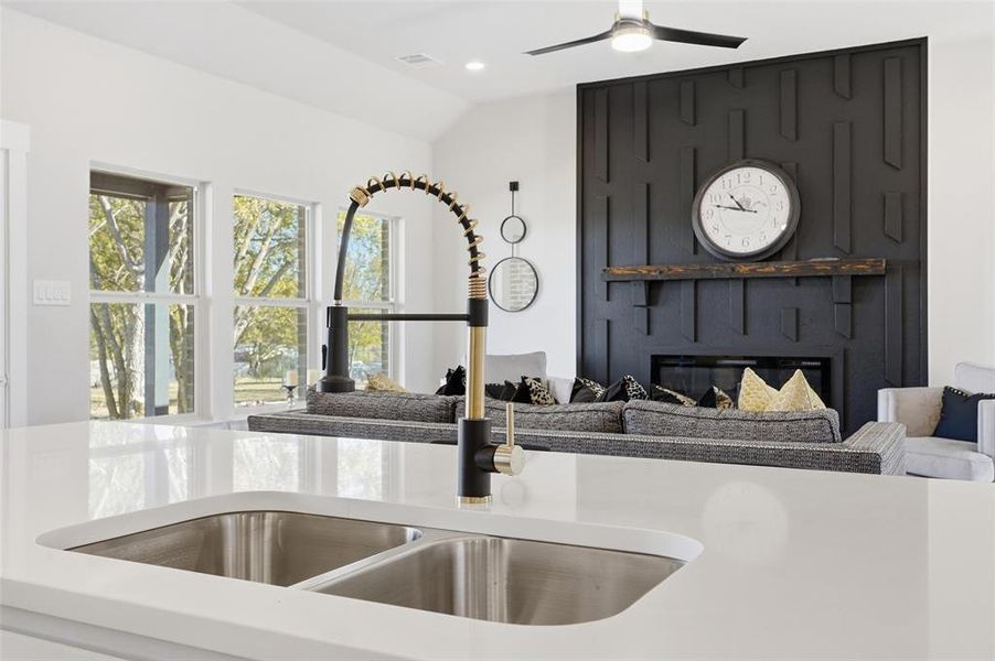 Kitchen view of a fireplace, light stone counters, and a ceiling fan