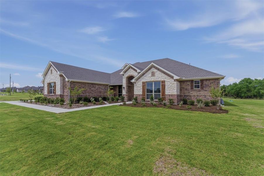 Brick and stone exterior featuring a gabled roofline, dark shingle roofing, decorative wooden window shutters, and a concrete walkway Brick and stone exterior featuring a gabled roofline, dark shingle roofing, decorative wooden window shutters, and a concrete walkway