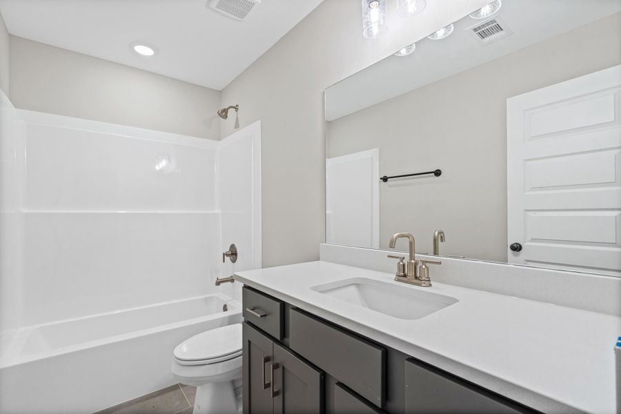 Bathroom featuring a white tub and shower combination, dark wood-finish vanity with a light-colored countertop, an undermount sink, and brushed nickel fixtures Bathroom featuring a white tub and shower combination, dark wood-finish vanity with a light-colored countertop, an undermount sink, and brushed nickel fixtures