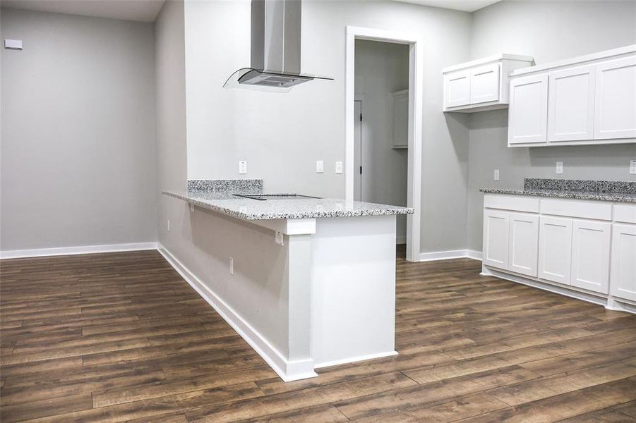 Kitchen featuring exhaust hood, dark wood finished floors, white cabinets, light stone countertops, and a peninsula