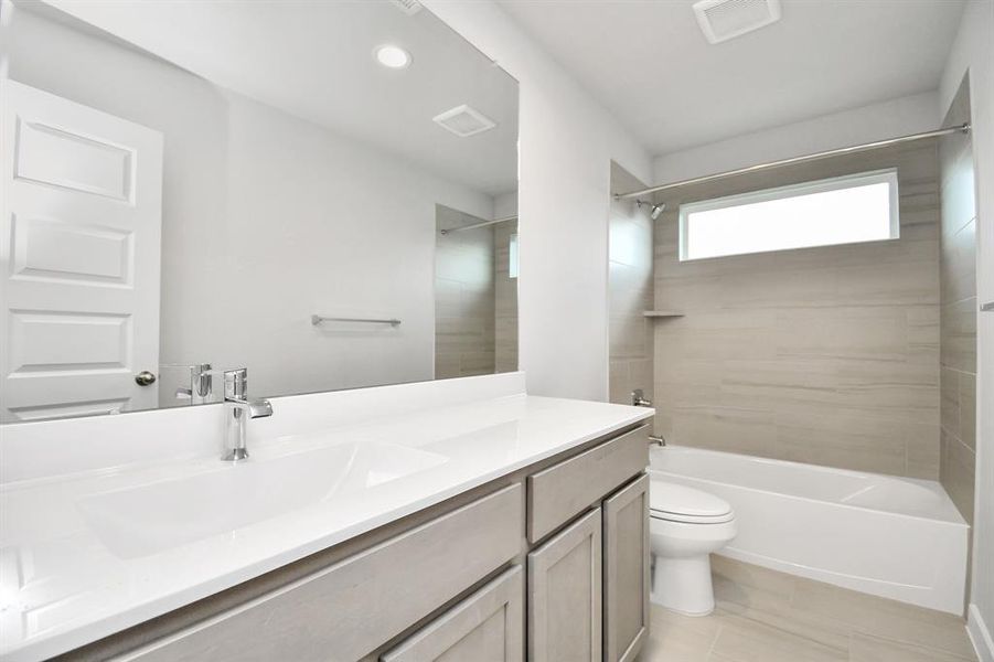 Secondary bath features tile flooring, bath/shower combo with tile surround, light stained wood cabinets, beautiful light countertop. Example photo of completed home with similar plan. Actual may vary.