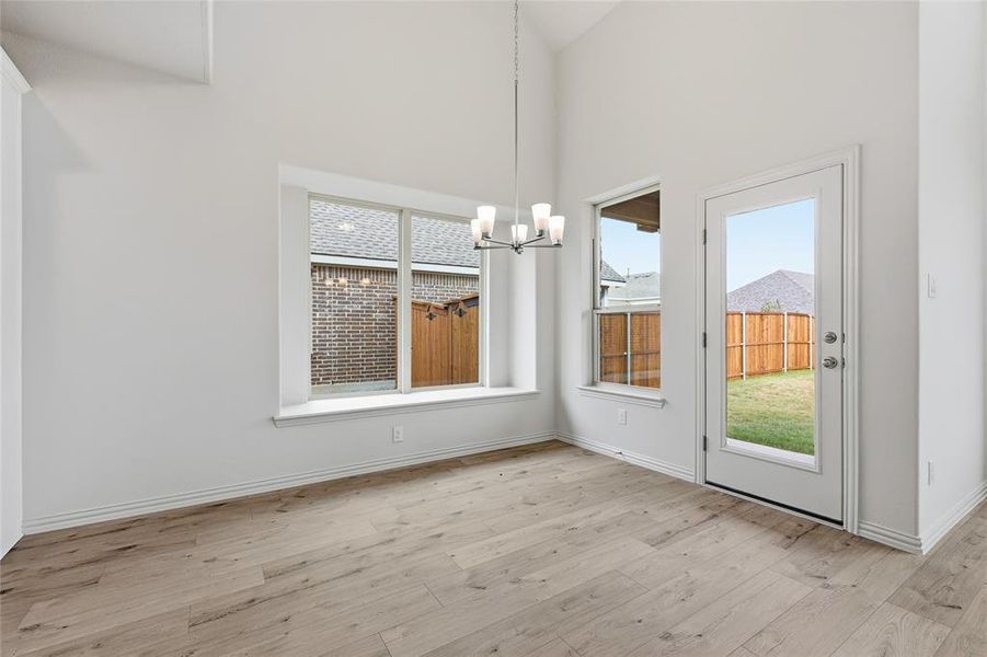 Unfurnished dining area with a chandelier, light wood-type flooring, and a towering ceiling Unfurnished dining area with a chandelier, light wood-type flooring, and a towering ceiling