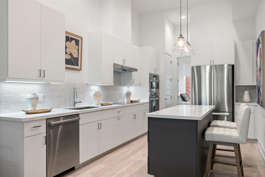 Kitchen with backsplash, light countertops, appliances with stainless steel finishes, a center island, and a towering ceiling