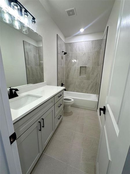 Full bathroom featuring tiled shower / bath combo, vanity, tile patterned floors, and toilet