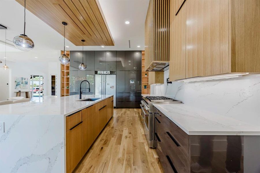 Kitchen featuring modern cabinets, light stone counters, a large island, high end range, and decorative light fixtures Kitchen featuring modern cabinets, light stone counters, a large island, high end range, and decorative light fixtures