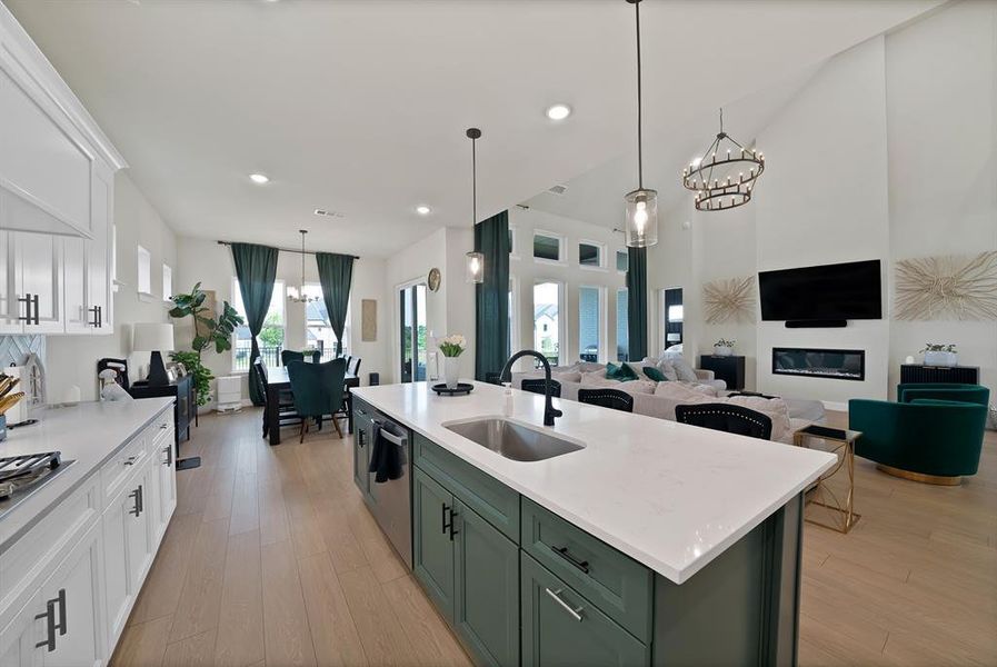 Open-concept living area featuring a kitchen island with sink and pendant lighting, wood-finish flooring, a dining area with direct outdoor access, a two-story living room with a linear fireplace, and large windows Open-concept living area featuring a kitchen island with sink and pendant lighting, wood-finish flooring, a dining area with direct outdoor access, a two-story living room with a linear fireplace, and large windows