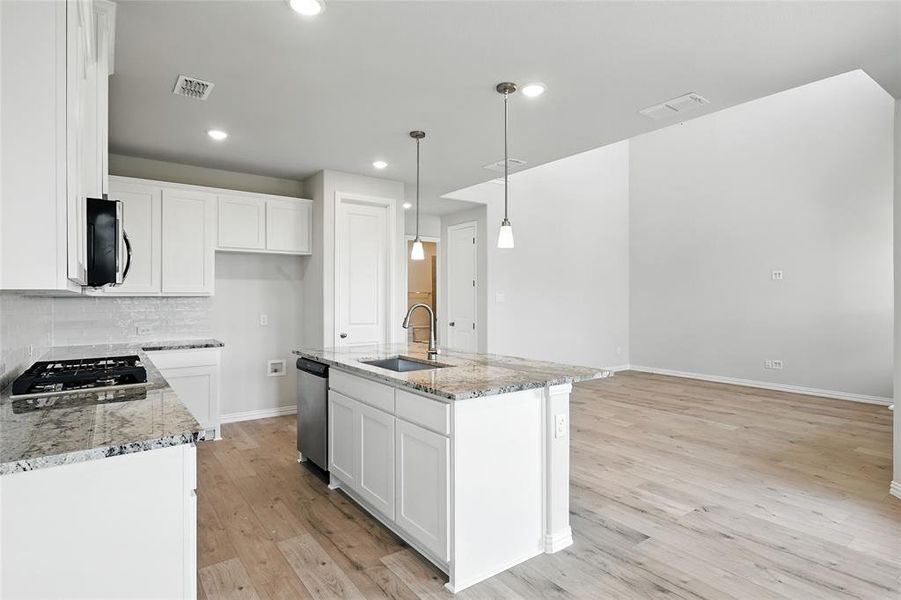 Kitchen with light stone countertops, light wood-style floors, white cabinets, decorative backsplash, and decorative light fixtures Kitchen with light stone countertops, light wood-style floors, white cabinets, decorative backsplash, and decorative light fixtures