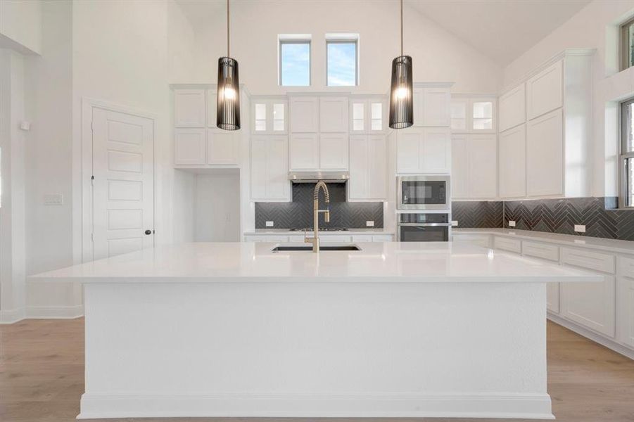 Contemporary kitchen featuring a large central island with an undermount sink, white cabinetry, integrated stainless steel appliances, and a dark herringbone tile backsplash Contemporary kitchen featuring a large central island with an undermount sink, white cabinetry, integrated stainless steel appliances, and a dark herringbone tile backsplash
