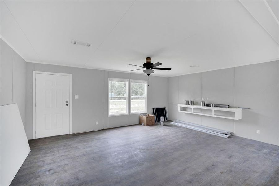 Spacious room featuring light gray walls, a white paneled entry door, and a black ceiling fan with light fixture