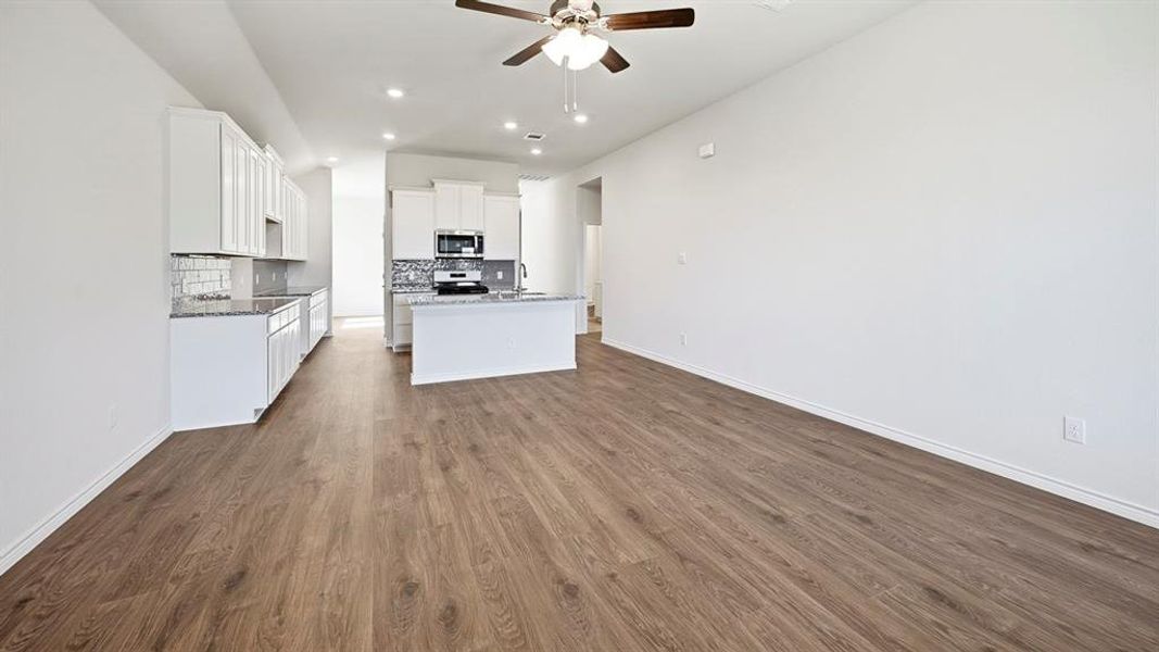 Kitchen with tasteful backsplash, white cabinetry, a center island with sink, ceiling fan, and open floor plan
