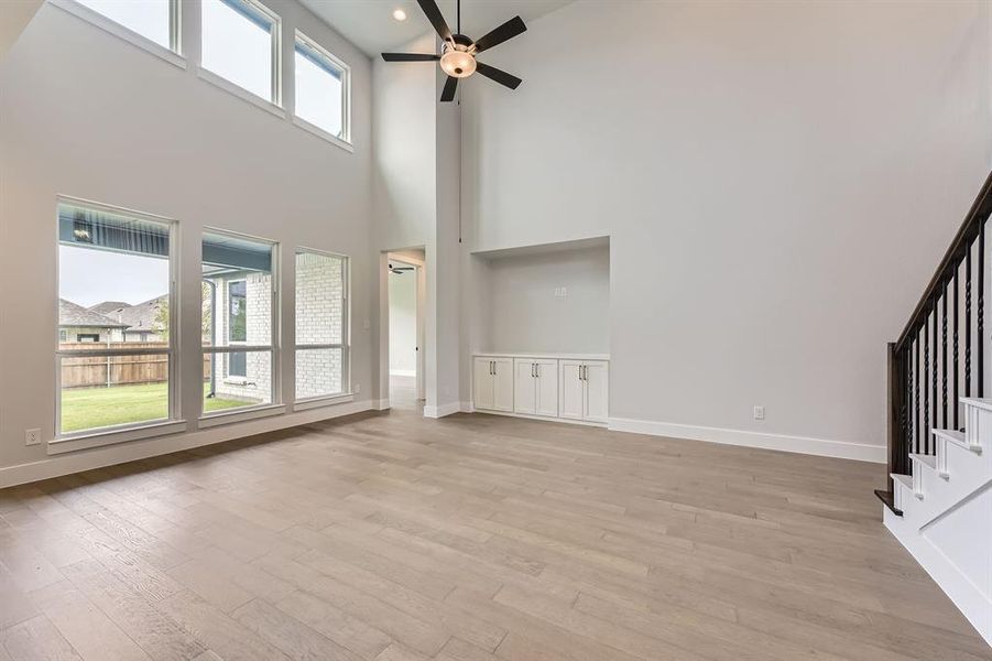 Unfurnished living room featuring a towering ceiling, ceiling fan, stairs, baseboards, and recessed lighting